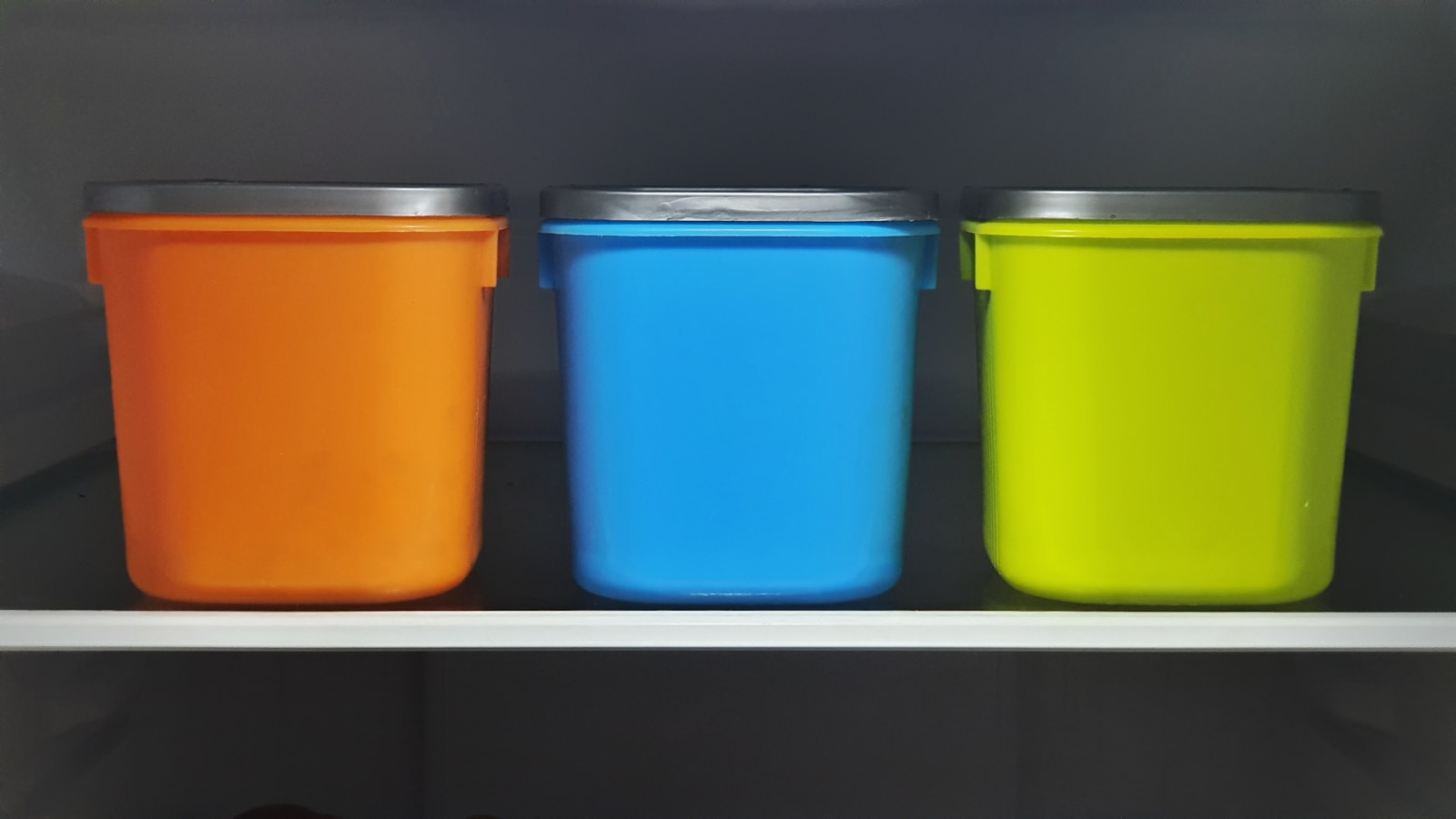 Three colorful lidded storage containers lined up on a shelf